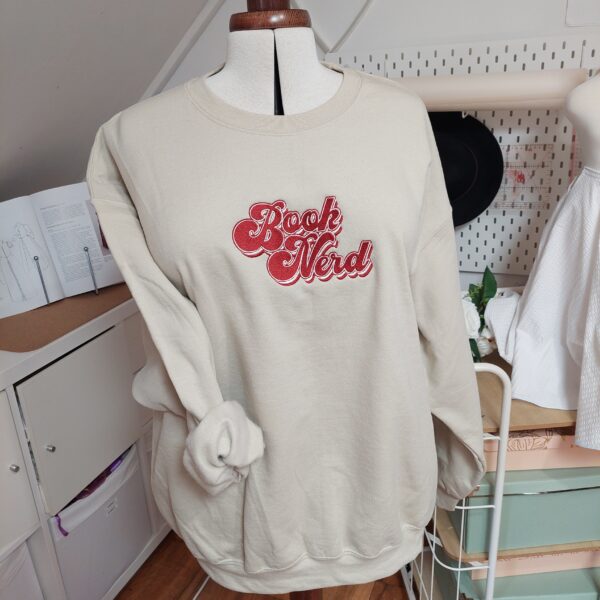 A cozy sweatshirt featuring the phrase "Book Nerd" prominently displayed on the chest. Perfect for book lovers!