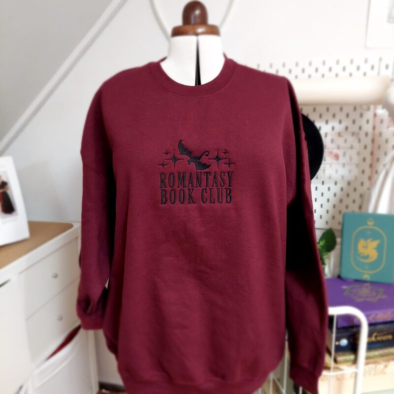 Cozy sweatshirts featuring the phrase "Romantasy Book Club" prominently displayed on the chest. Perfect for book lovers!